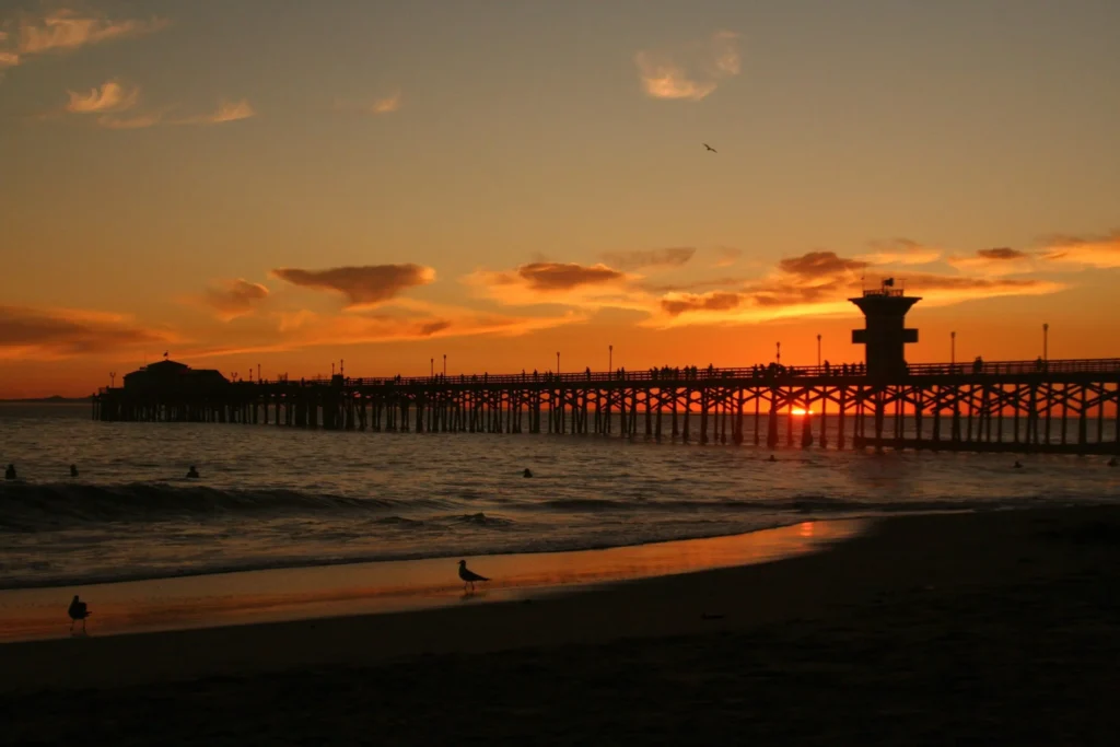 A serene sunset casts vibrant hues over the calm ocean, reflecting warm colors on the water's surface.